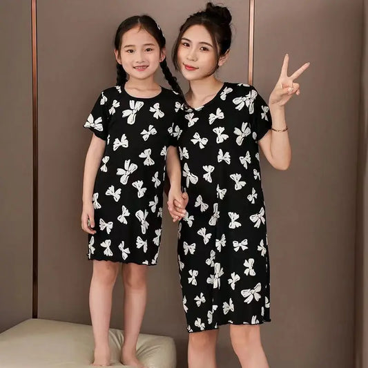 Two people wearing a girls black cotton nightdress with white butterfly print and short sleeves