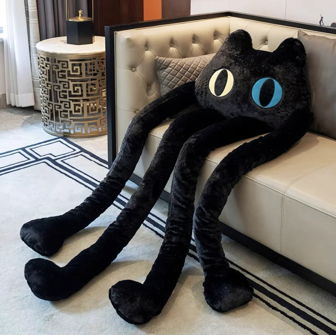 Black long-legged cat plush toy resting on a sofa with extended arms and legs