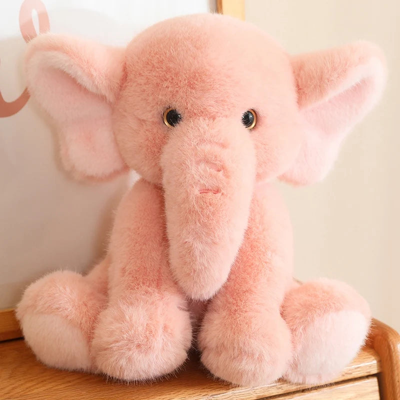 Pink soft plush elephant toy sat on a wooden surface, with a white background.