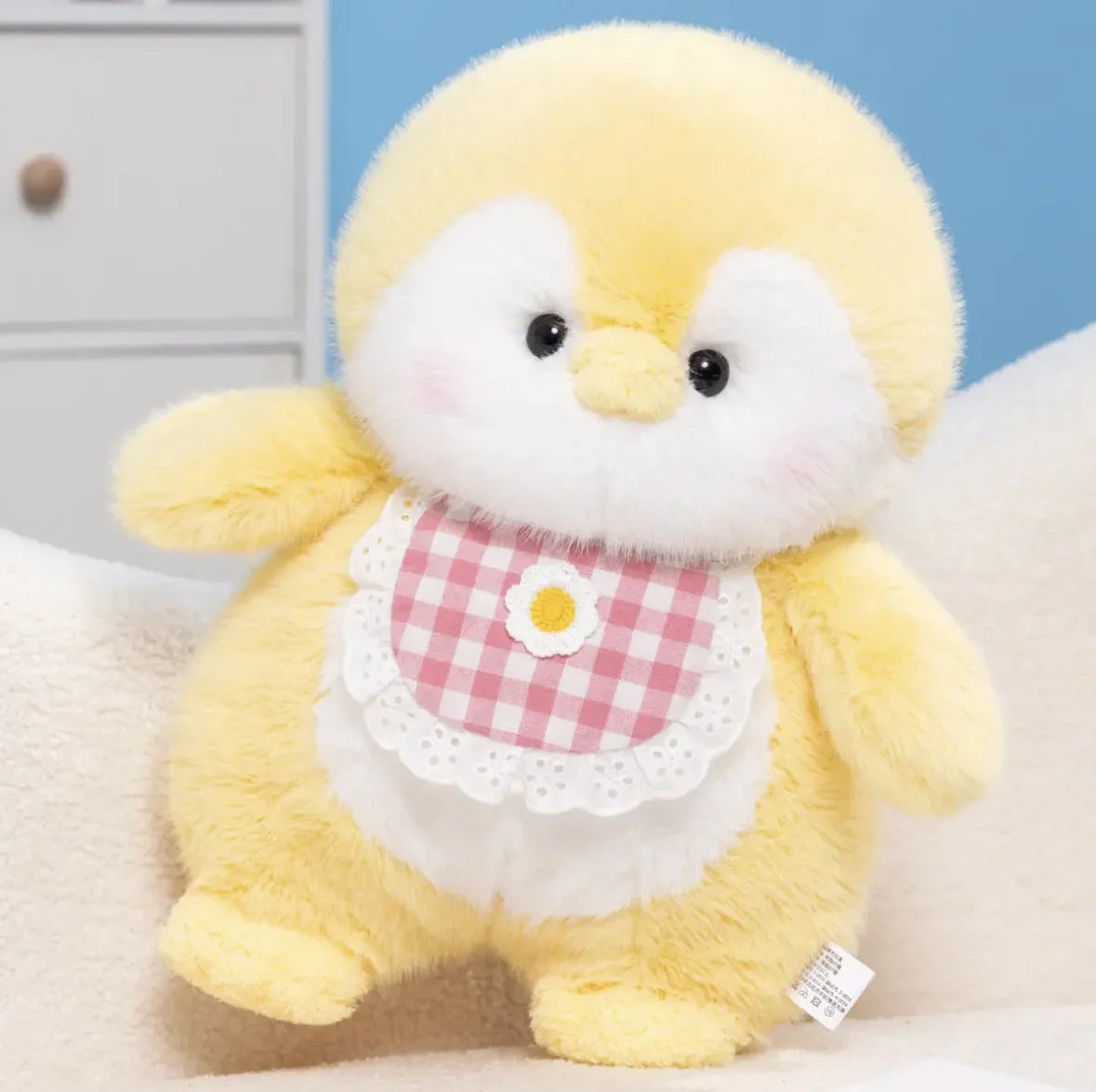 Yellow plush toy with a checkered bib on a bedroom setting.
