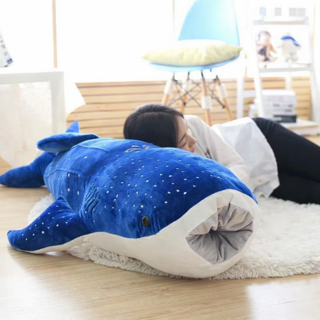 Blue soft plush whale toy with a open mouth lying on a white rug in a cosy room.