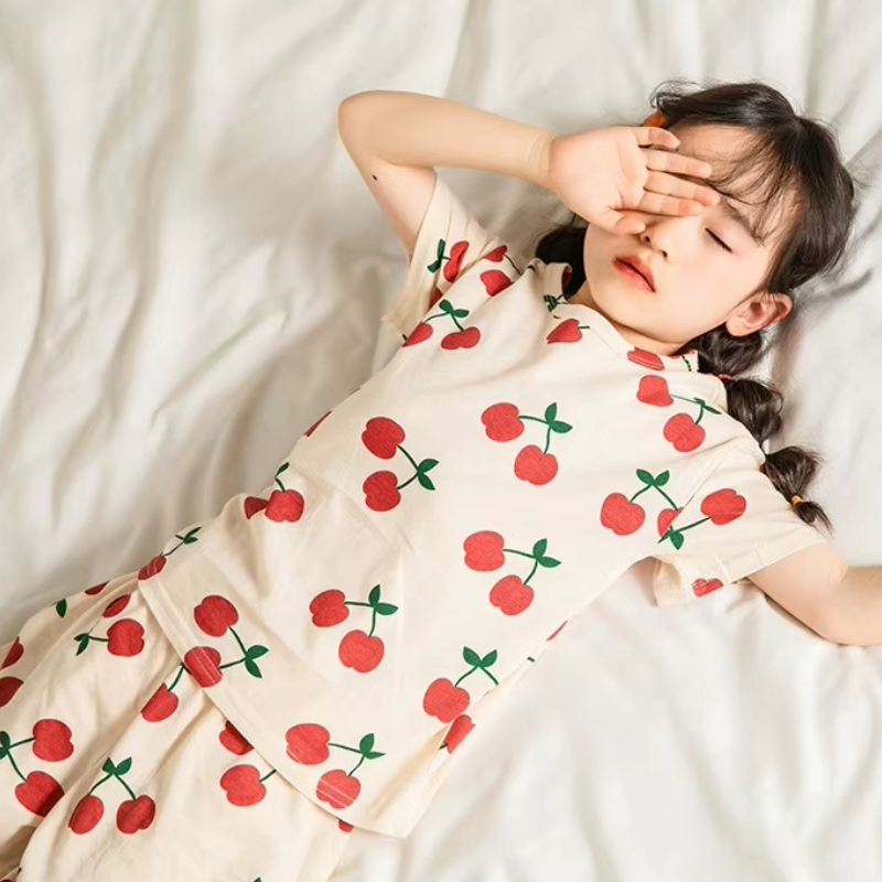 Child lying down wearing a cherry print pyjama set in a cosy setting