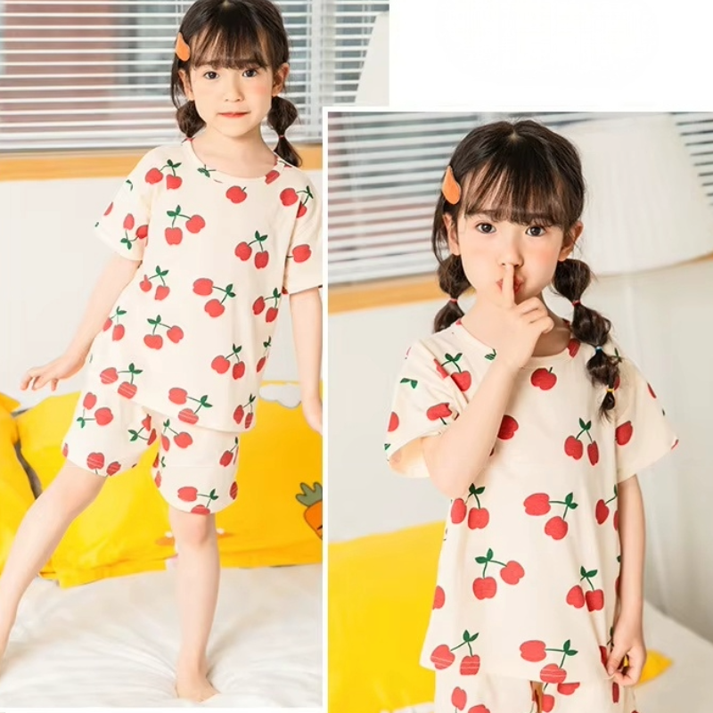 Two images of a child wearing a cherry print pyjama set in a cosy settings
