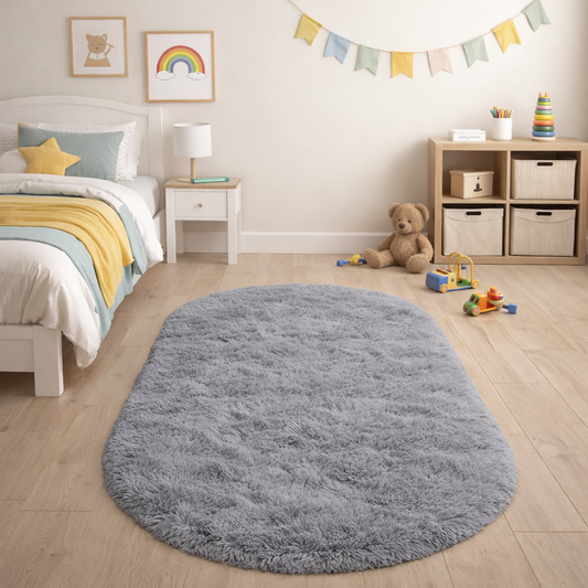 Soft grey silky plush oval rug shown beside a bed in a calm neutral room