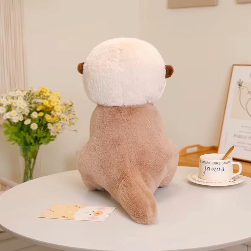 Otter soft toy shown from the back, with a soft brown plush body and white head, displayed on a table