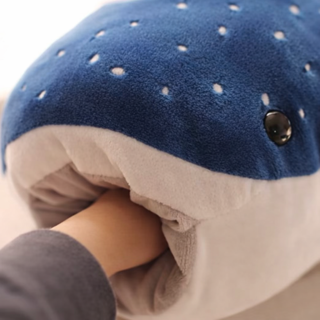 Close up of a blue soft plush whale with a fist in its mouth.