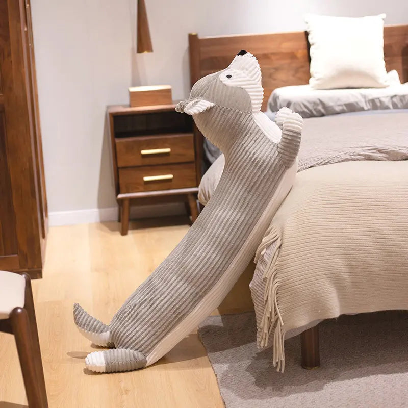 Grey husky long body plush sleeping companion resting against a bed with extended shape