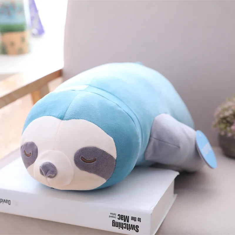 Blue soft plush sloth toy resting on a book in a cosy setting.