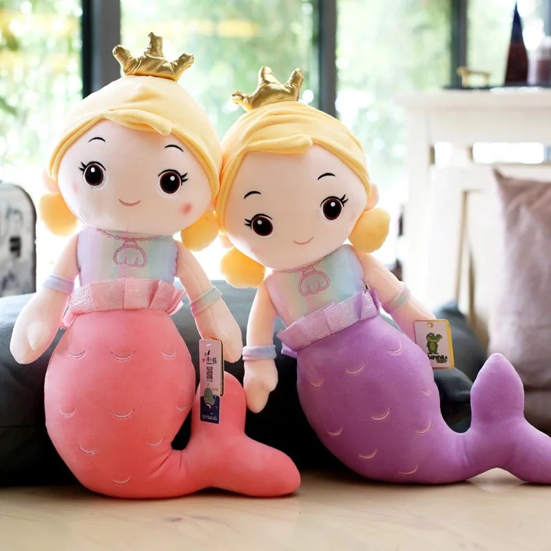 Two plush toys resembling mermaids with crowns on a blurred indoor background
