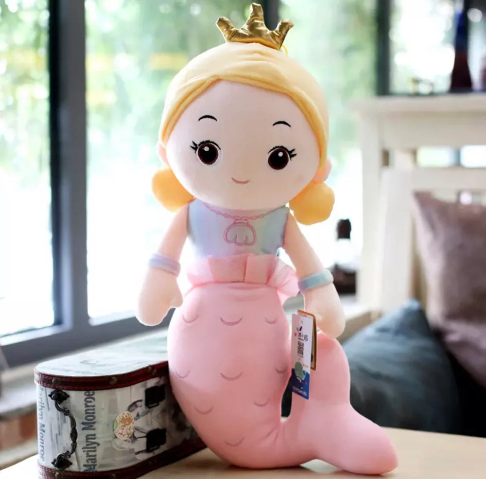 Plush toy mermaid with a princess crown on a table in front of a window