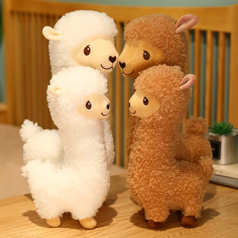 Four plush alpaca toys in white, and brown on a wooden surface.