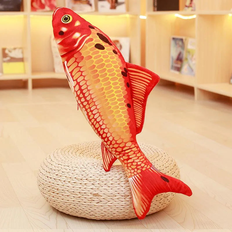 Bright orange koi fish soft toy with scale pattern and fins, displayed upright on a round woven stand