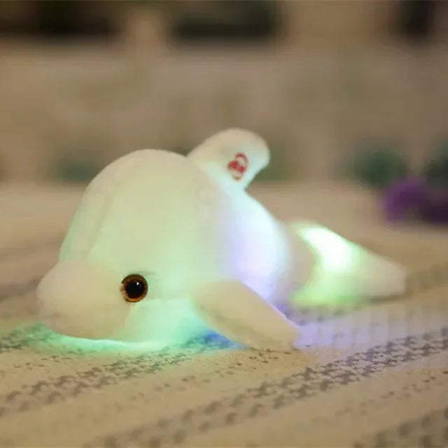 White soft plush light-up dolphin on a blurred surface.