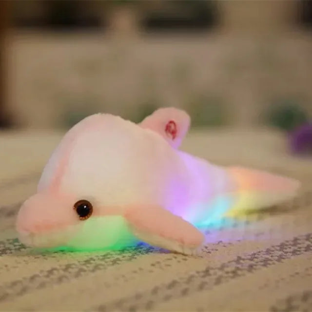 Pink soft plush light-up dolphin on a blurred surface.