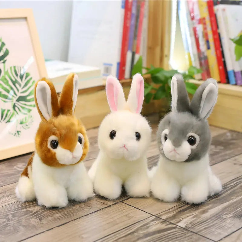 Three plush rabbit toys in brown, white, and grey sitting on a wooden floor.