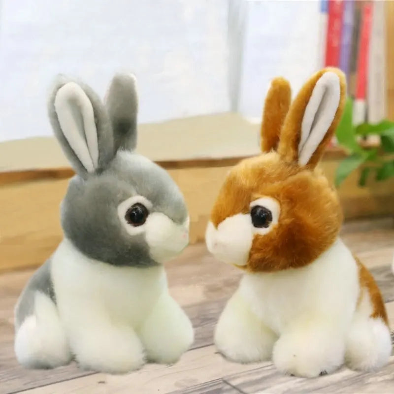 Two plush rabbit toys, one grey and one brown and white, on a wooden surface.