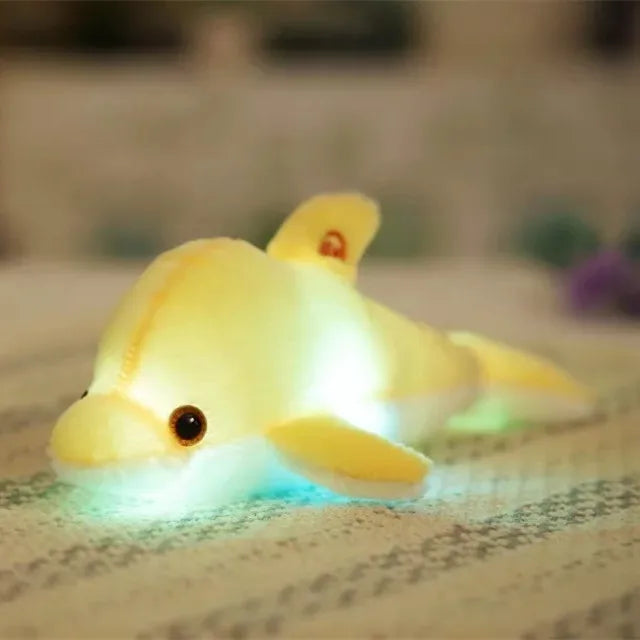 Yellow soft plush light-up dolphin on a blurred surface.