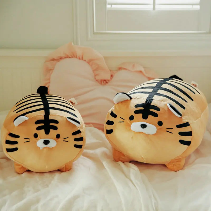 Round tiger plush toy with soft printed stripes displayed in two size options on a bed