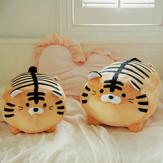 Round tiger plush toy with soft printed stripes displayed in two size options on a bed