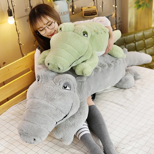 Woman holding a large green and larger grey soft plush crocodile toy.
