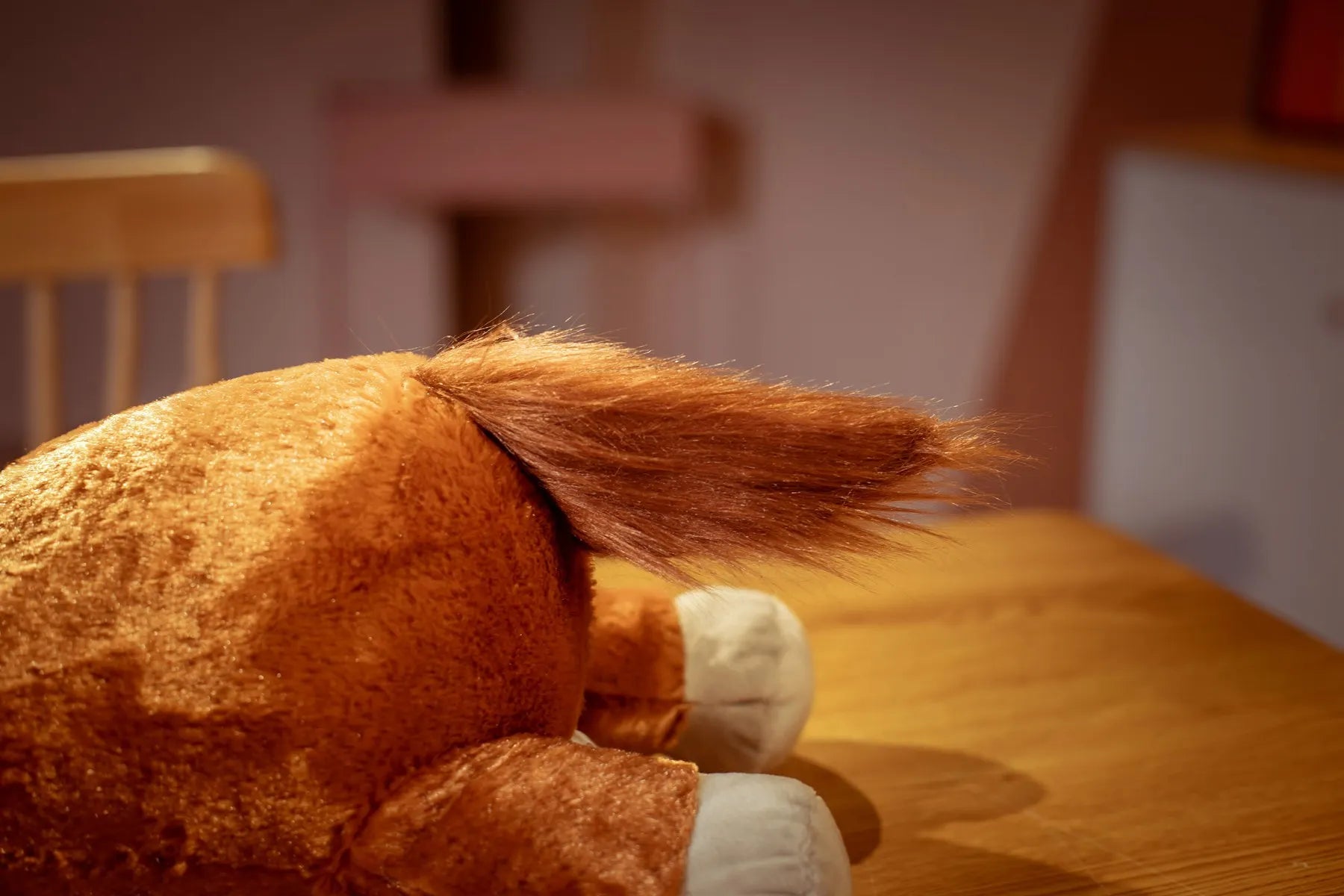 Close-up of a tail of a plush horse toy on a wooden table.