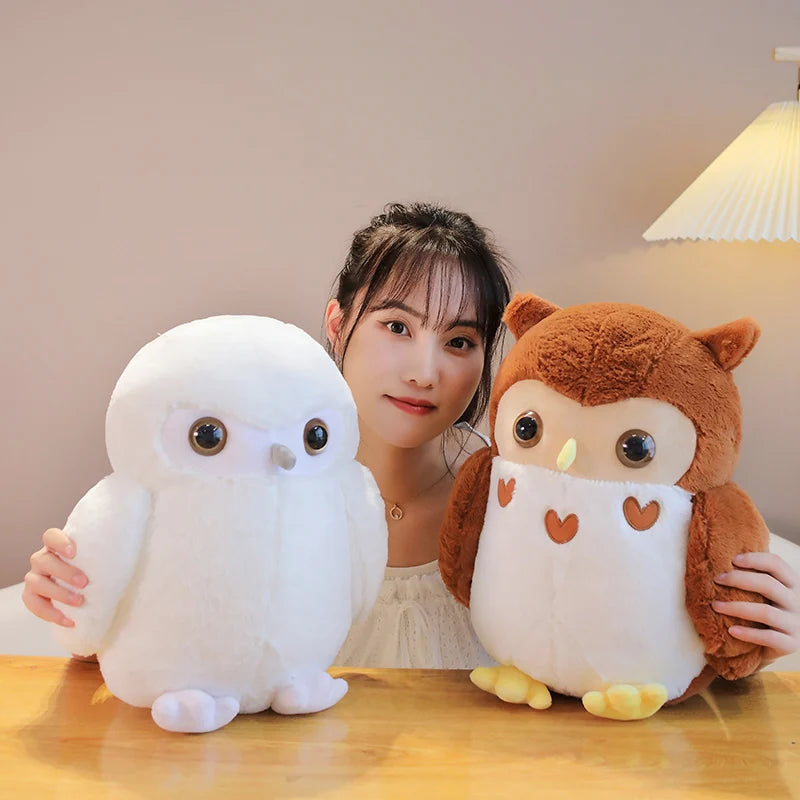 Woman holding two plush owl toys on a wooden table.
