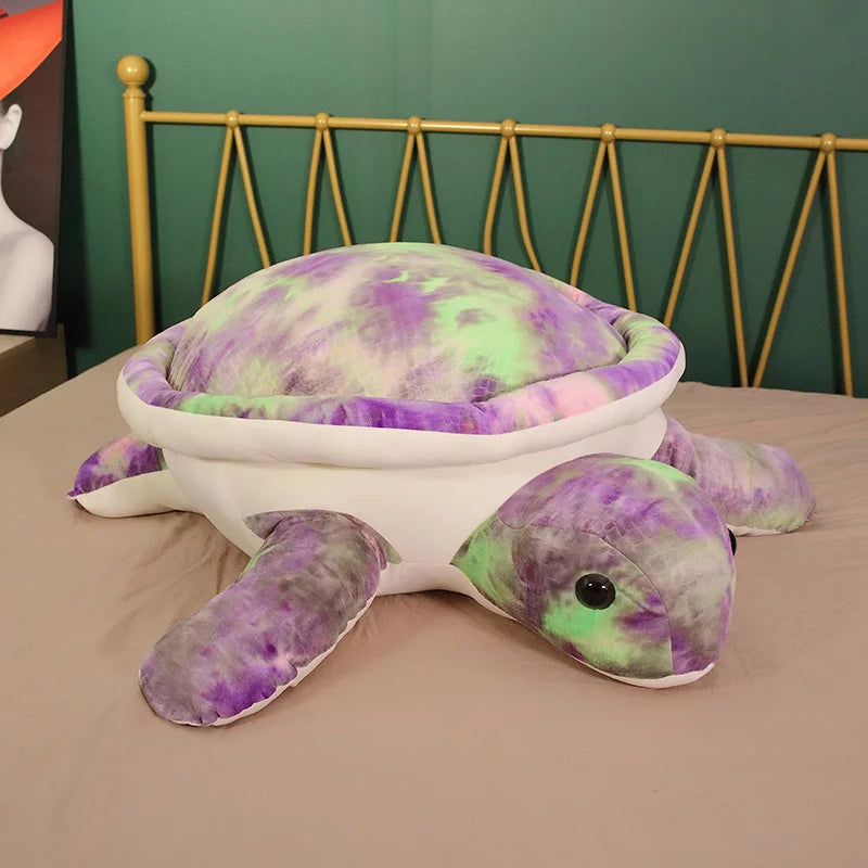 Multicoloured tie dye soft plush turtle toy on a bed.
