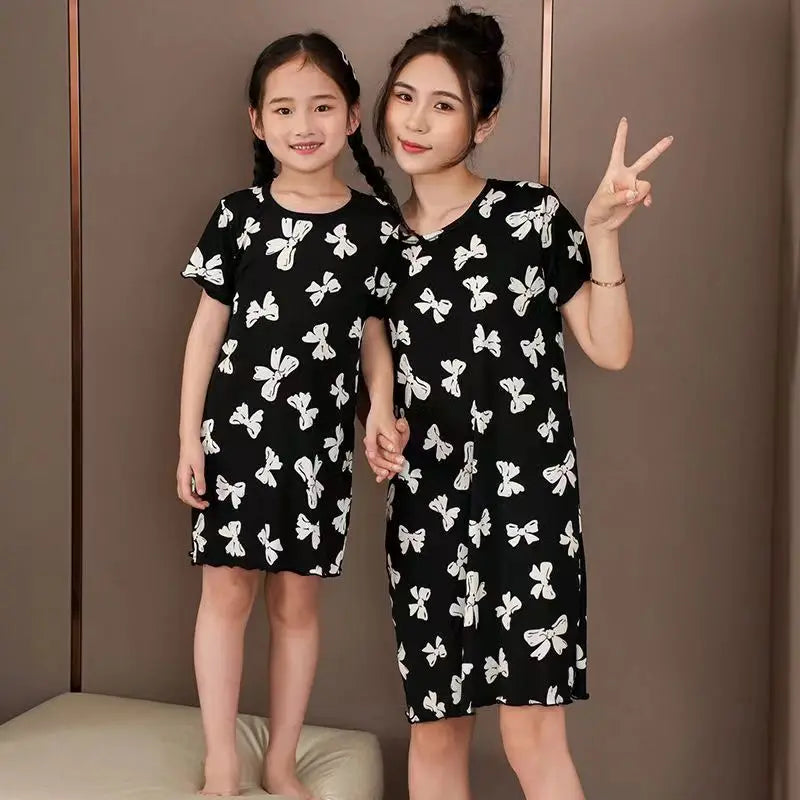 Two people wearing a girls black cotton nightdress with white butterfly print and short sleeves