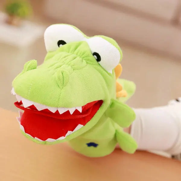 Green plush hand puppet, resembling a crocodile, held by a hand.