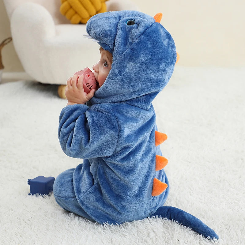 Baby in a blue dinosaur onesie sitting on a white surface.