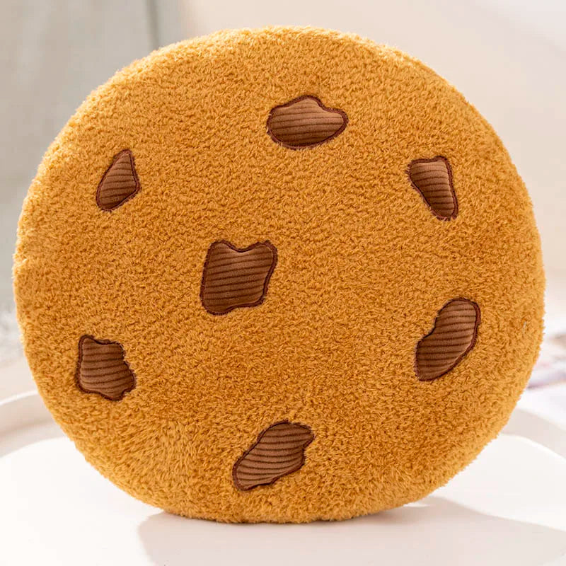 Round chocolate chip cookie soft toy cushion with a smiling face and raised cookie pieces on a plain background