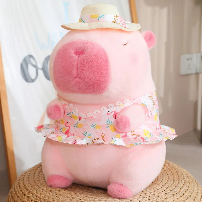 Pink capybara plush soft toy wearing a patterned dress and hat with a calm, sleepy expression
