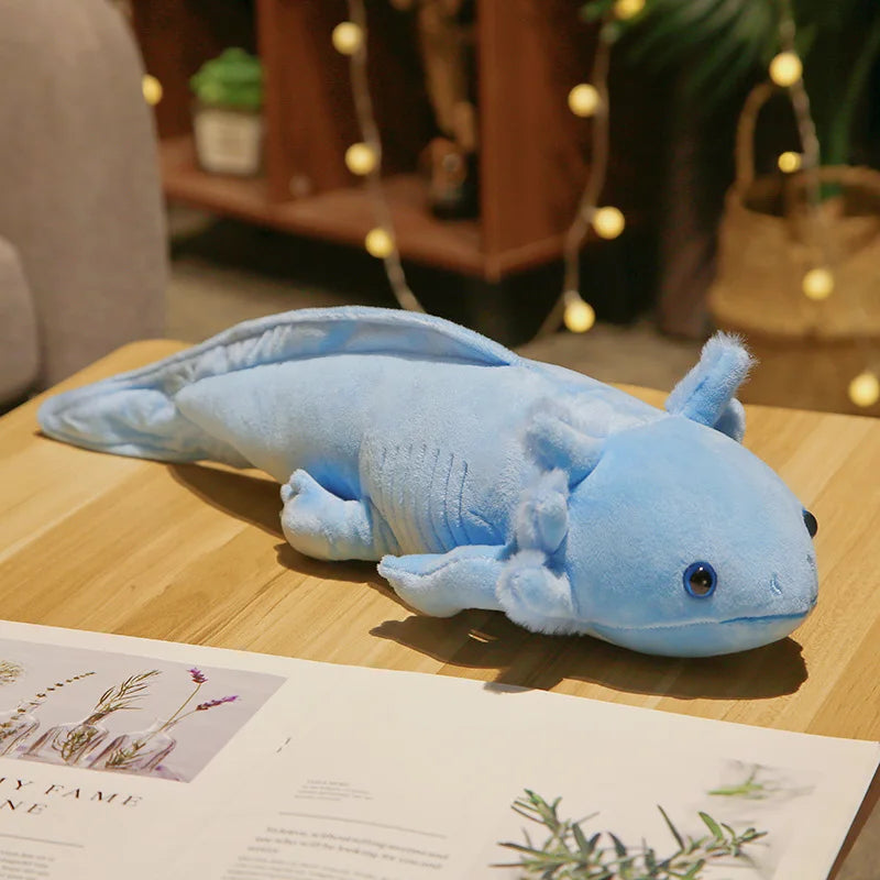 Blue axolotl plush toy on a wooden surface with a magazine underneath
