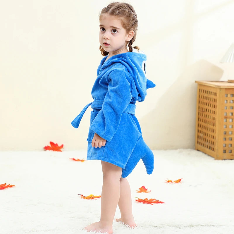 Child wearing a blue hooded robe on a white floor with decorative orange leaves.
