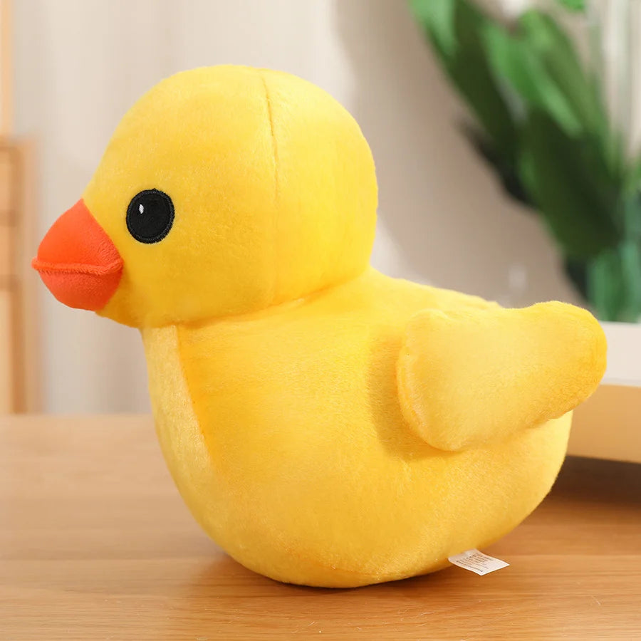 Yellow duck plush toy with an orange beak and small wings, shown in side view on a wooden surface