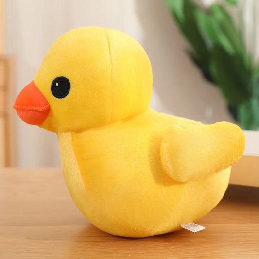Yellow duck plush toy with an orange beak and small wings, shown in side view on a wooden surface
