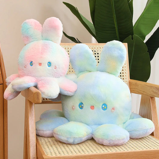 Two pastel-coloured plush toys on a wooden chair with a plant in the background