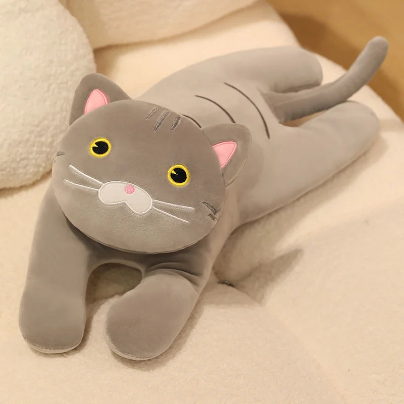 Grey cat soft toy with yellow eyes and a soft plush finish, reclining on a cream sofa