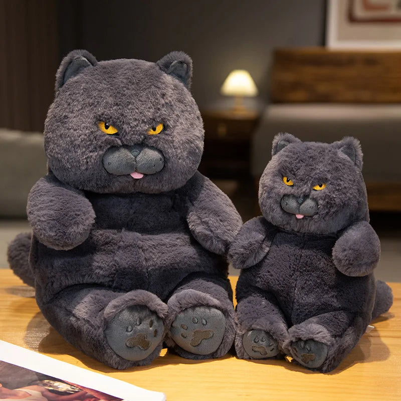 Two grey plush lazy cats sitting on a wooden surface with a blurred indoor background.
