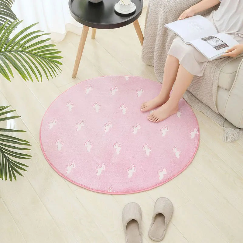 Round pink printed kids rug placed on a light wood floor beside a sofa
