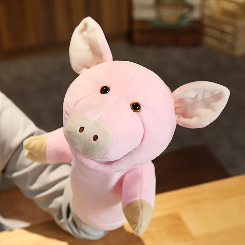 Pink plush pig hand puppet held by a person on a wooden surface.
