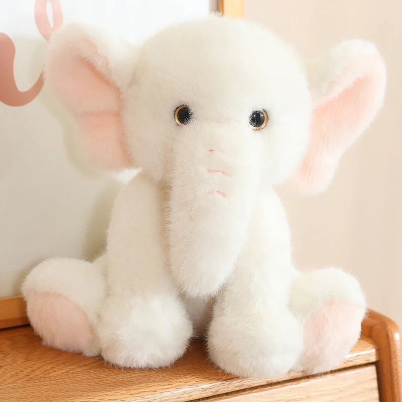 White soft plush elephant toy sat on a wooden surface, with a white background.