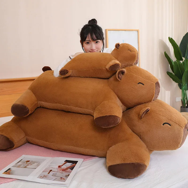 Three different sized capybara plush toys, with a woman behind for comparison.