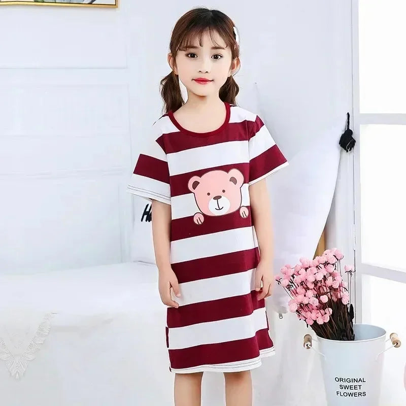 Child wearing a red and white striped nightie with a bear design, standing in a room with a white wall and a small plant.