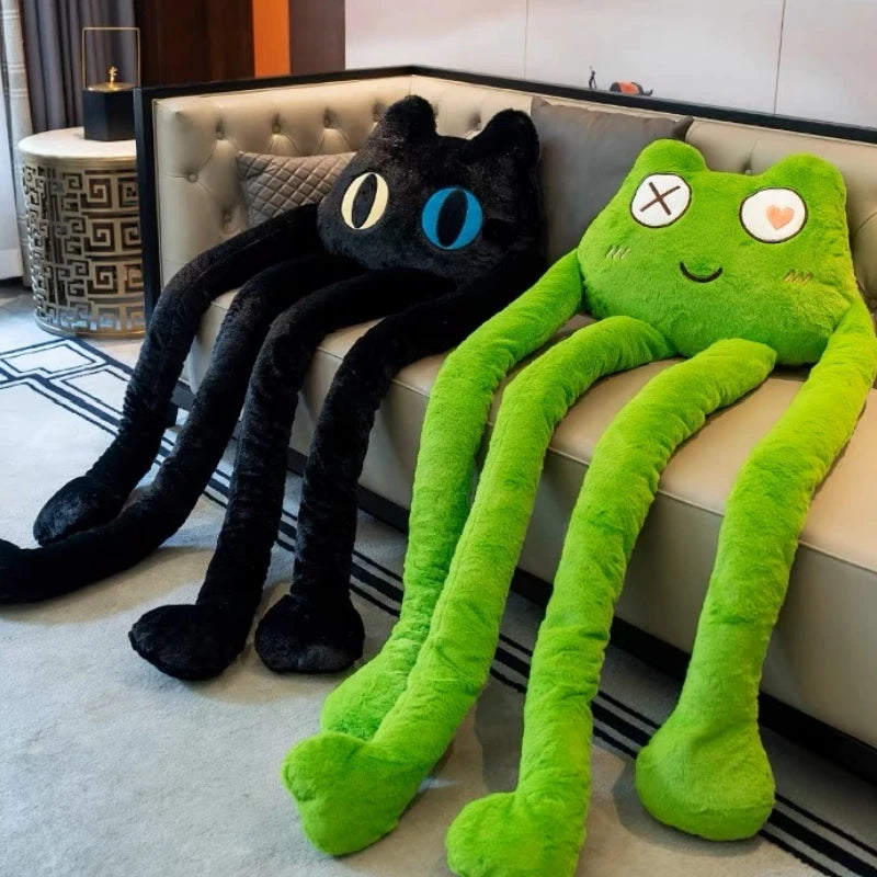 Two plush toys, one black cat and one green frog, on a couch.