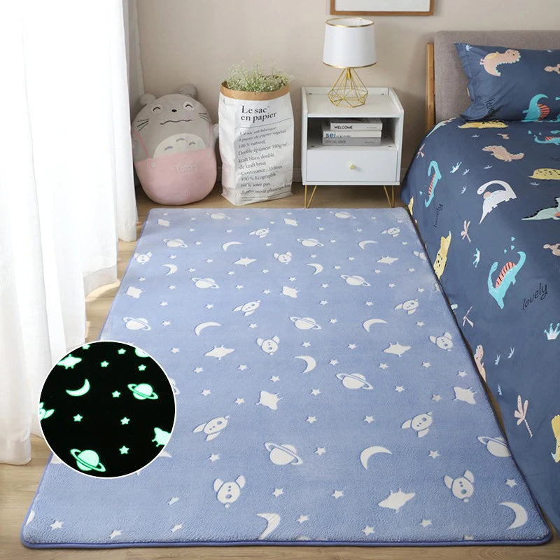 Blue plush children's rug with white rockets and stars placed on the floor beside a bed