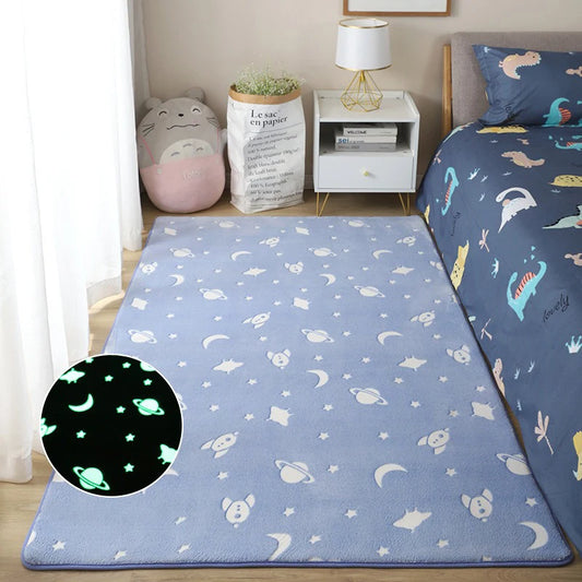 Blue plush children's rug with white rockets and stars placed on the floor beside a bed