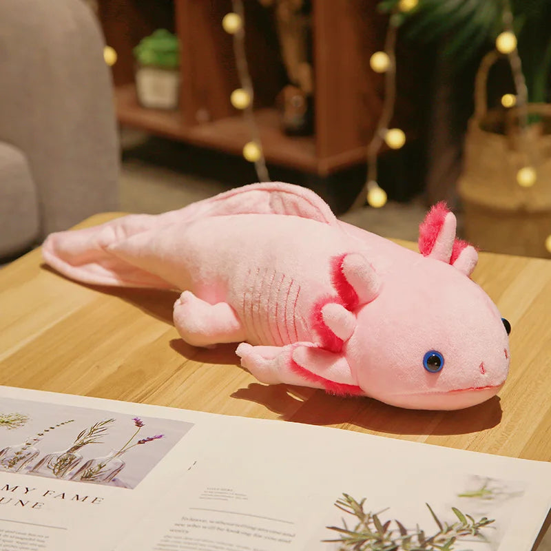 Pink axolotl plush toy on a wooden table with a magazine underneath