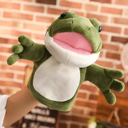 Plush frog hand puppet held by a person against a brick wall background