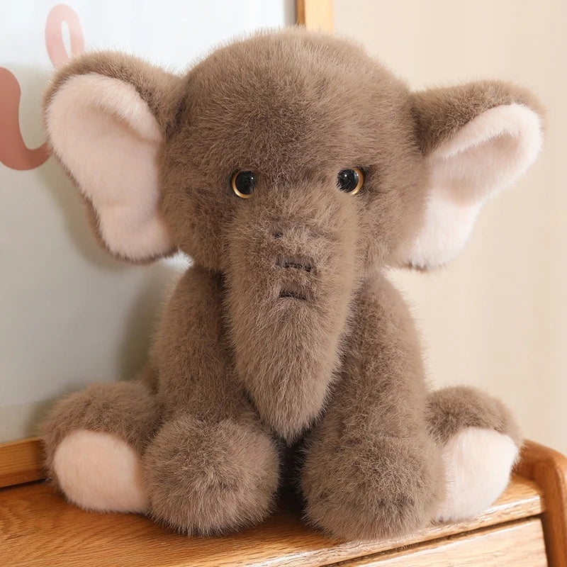 Grey soft plush elephant toy sat on a wooden surface, with a white background.